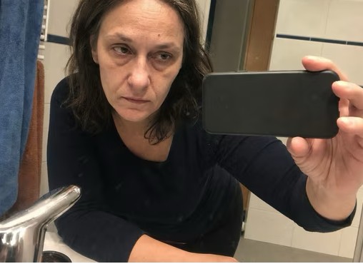 A woman in her fifties photographing her reflection in a bathroom mirror