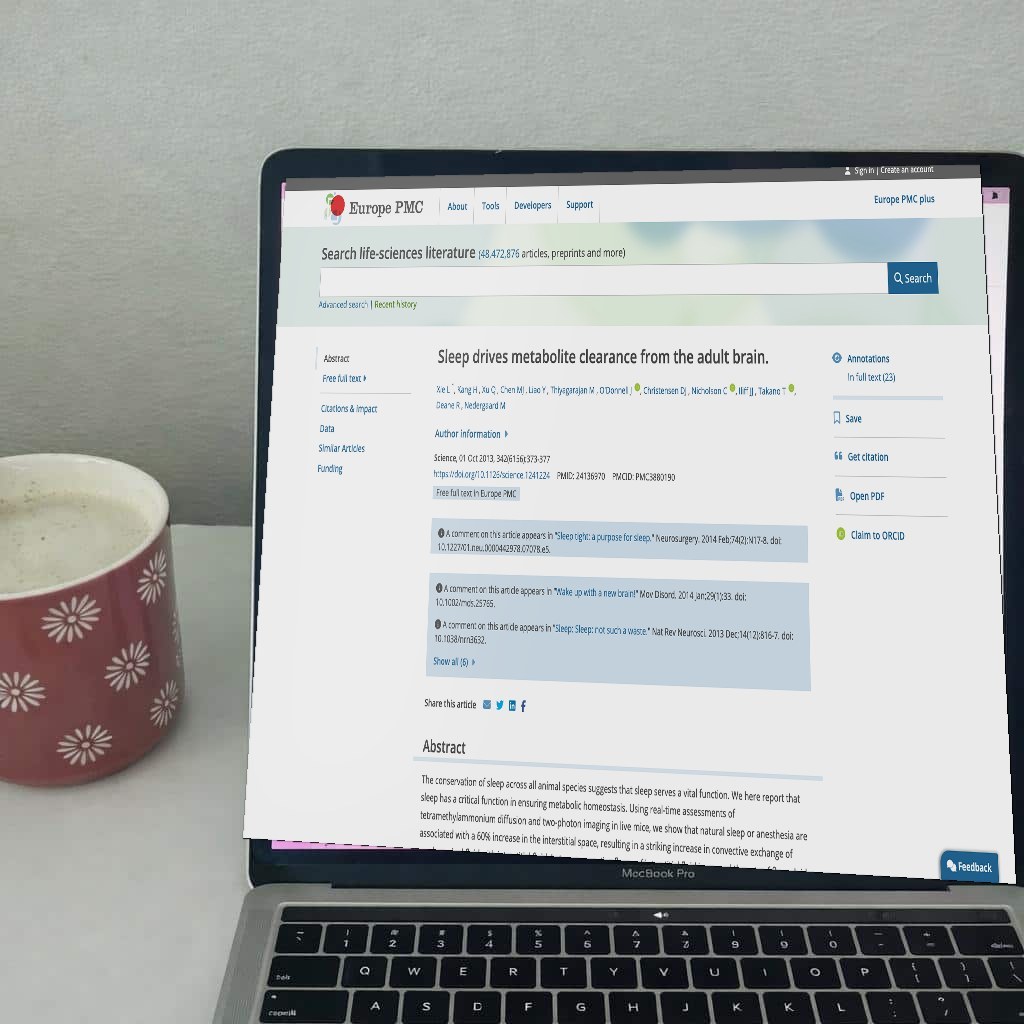 A laptop open on a desk showing a sleep and brain research paper, with a coffee mug beside it